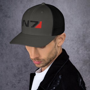 May include: A dark gray and black trucker hat with a red and black N7 logo embroidered on the front.