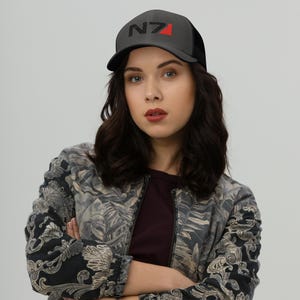 May include: A black and red trucker hat with the text "N7" embroidered on the front. The hat is worn by a person with long black hair.
