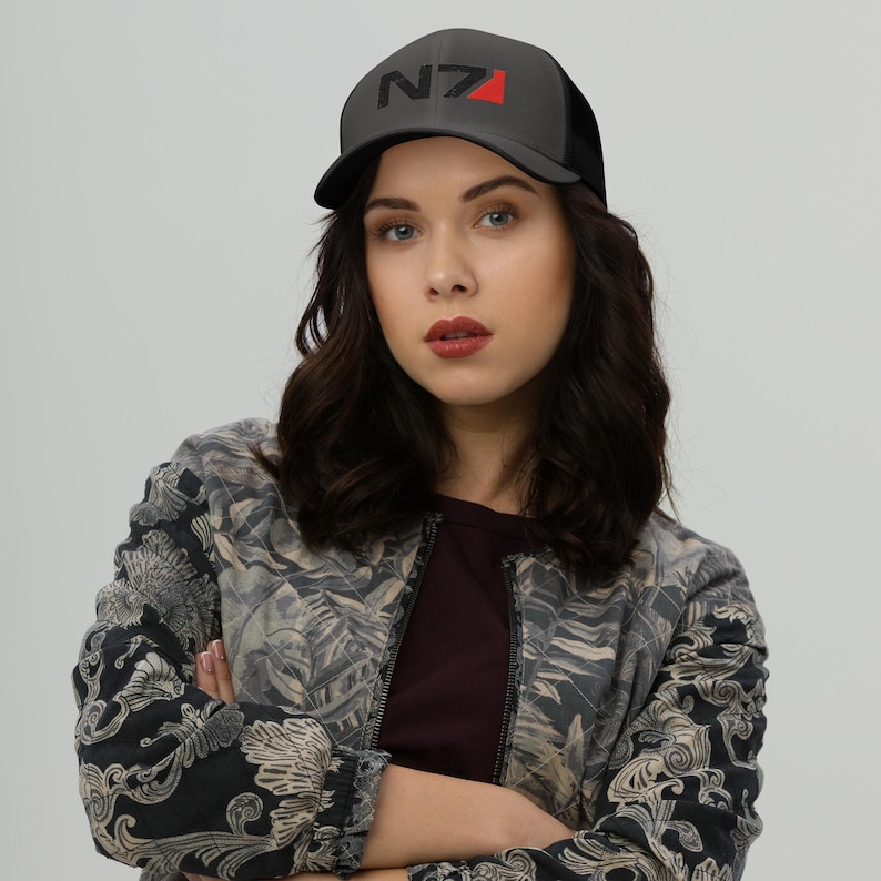 May include: A black and red trucker hat with the text "N7" embroidered on the front. The hat is worn by a person with long black hair.