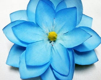 Könnte beinhalten: Ein Stoffblumen-Accessoire mit mehreren Schichten leuchtend blauer Blütenblätter, die zur Mitte hin heller werden. In der Mitte der Blume befindet sich ein kleiner, texturierter gelber Staubfaden. Der Text Silvergirl und 12-08 ist sichtbar.