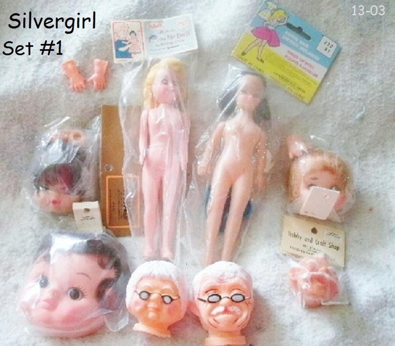 May include: A set of doll parts, including heads, bodies, and hands. The doll parts are made of plastic and are in various colours, including pink, white, and brown. The set is labelled "Silvergirl Set #1".