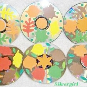 Puede incluir: Seis CDs con hojas de otoño pintadas en varios tonos de naranja, amarillo, marrón y verde. Las hojas están dispuestas en un patrón circular en cada CD.
