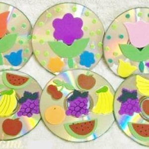 Puede incluir: Seis CDs coloridos con diferentes diseños de frutas y flores hechos con espuma. Los diseños incluyen una sandía, uvas, un plátano, una manzana, una flor y un tulipán.