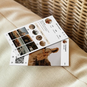 May include: Two white business cards with a travel theme. One card displays a mock Instagram profile with travel photos and the handle @travelagent. The other card shows a photo of a person in a hat. The cards are on a beige surface.