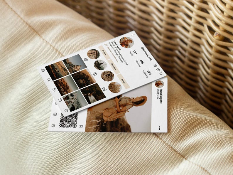 May include: Two white business cards with a travel theme. One card displays a mock Instagram profile with travel photos and the handle @travelagent. The other card shows a photo of a person in a hat. The cards are on a beige surface.