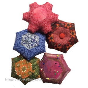 May include: A collection of handmade, colorful pincushions in various shapes and patterns. The pincushions feature floral and geometric designs in shades of red, blue, green, and orange. Some have pins inserted, indicating their use for sewing and crafting.