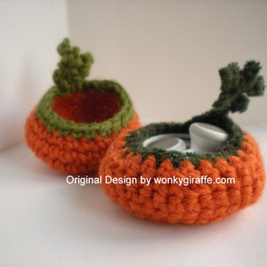 May include: Two small, round, orange crocheted containers with dark green rims and leafy tops. The front container holds white buttons. The text Original Design by wonkygiraffe.com is printed across the center of the image in white letters.