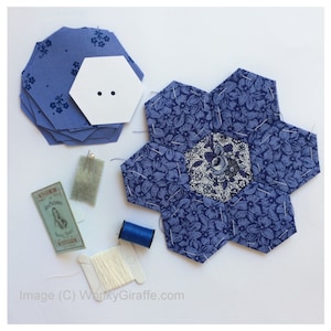 May include: A collection of quilting supplies, including blue floral fabric hexagons, a white paper hexagon, pins, thread, and a spool of white thread. The fabric features a blue floral pattern. The image suggests a crafting or sewing project.