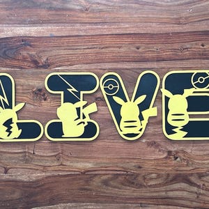 May include: Black and yellow wooden letters spelling the name "OLIVER" with a Pikachu character design on each letter.