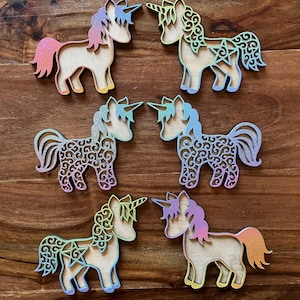 May include: Six wooden unicorn ornaments with intricate designs and a rainbow glitter finish. The unicorns are standing on a wooden surface.