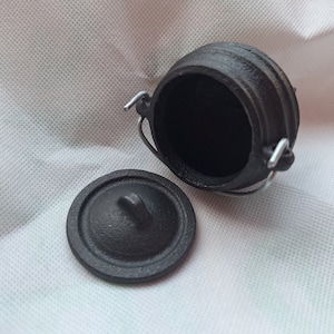 May include: A small black cast iron pot with a lid and a handle. The pot is empty and the lid is off.
