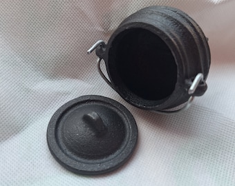 May include: A small black cast iron pot with a lid and a handle. The pot is empty and the lid is off.