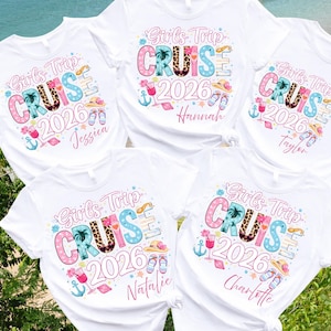May include: Five white t-shirts featuring a colorful graphic with the text Girls Trip CRUISE 2026. The design includes tropical icons like palm trees, cocktails, anchors, sun hats, and flip-flops, with individual names printed below the year.