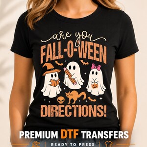 May include: A black short-sleeve t-shirt featuring a graphic print with the text "are you FALL-O-WEEN DIRECTIONS!". The design includes three white ghosts, one wearing a witch hat, one holding a pencil, and one with a pink bow, plus a cat and skull.