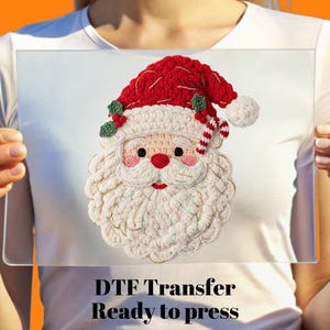 May include: A DTF transfer featuring a detailed Santa Claus design. The image shows a red hat, white beard, and rosy cheeks. The text "DTF Transfer Ready to press" is visible at the bottom.