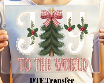 May include: A clear rectangular sign with the words "JOY TO THE WORLD" in a festive design. The word "JOY" is in white with lace accents and holly berries. A Christmas tree and a red plaid bow are in the center.