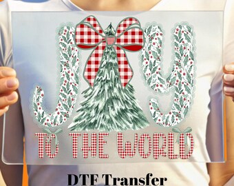 May include: A clear rectangular DTF transfer with a Christmas design. The design features the words "JOY TO THE WORLD" in red and green, with a Christmas tree and bow. The transfer is ready to press.