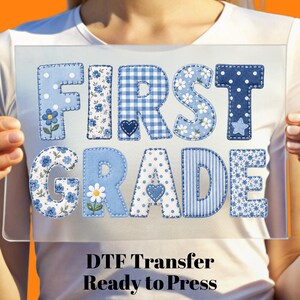 May include: A DTF transfer sheet featuring the text FIRST GRADE in large, block-style letters. The letters are decorated with various blue and white patterns, including gingham, polka dots, stripes, and floral prints, with small heart and star accents.