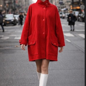 May include: A bright red coat with a high collar and large pockets. The coat is buttoned up and worn with white boots and a white hat. The coat appears to be made of a wool or wool-blend fabric.