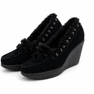May include: A pair of black wedge heel shoes with a moccasin-style design. The shoes feature a suede-like texture, faux fur trim, and decorative bows. The heels are approximately 3 inches high.