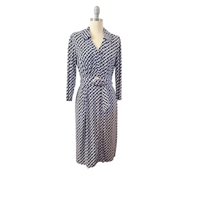 May include: A long-sleeved, midi-length dress in a black and white geometric pattern. The dress features a collared neckline, a cinched waist with a silver-toned buckle, and a flowing skirt. The dress is displayed on a mannequin.