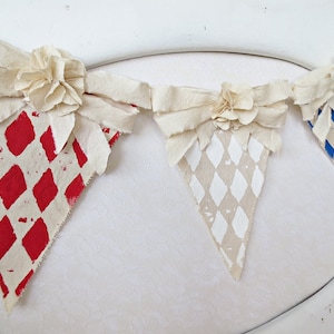 May include: A fabric banner with three triangular flags. Each flag has a different diamond pattern in red, white, and blue. The flags are connected with white fabric bows.