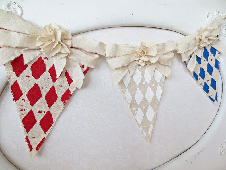May include: A fabric banner with three triangular flags. Each flag has a different diamond pattern in red, white, and blue. The flags are connected with white fabric bows.