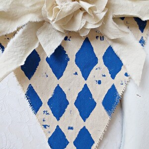 May include: A white fabric banner with a blue diamond pattern. The banner has a white fabric flower attached to the top.