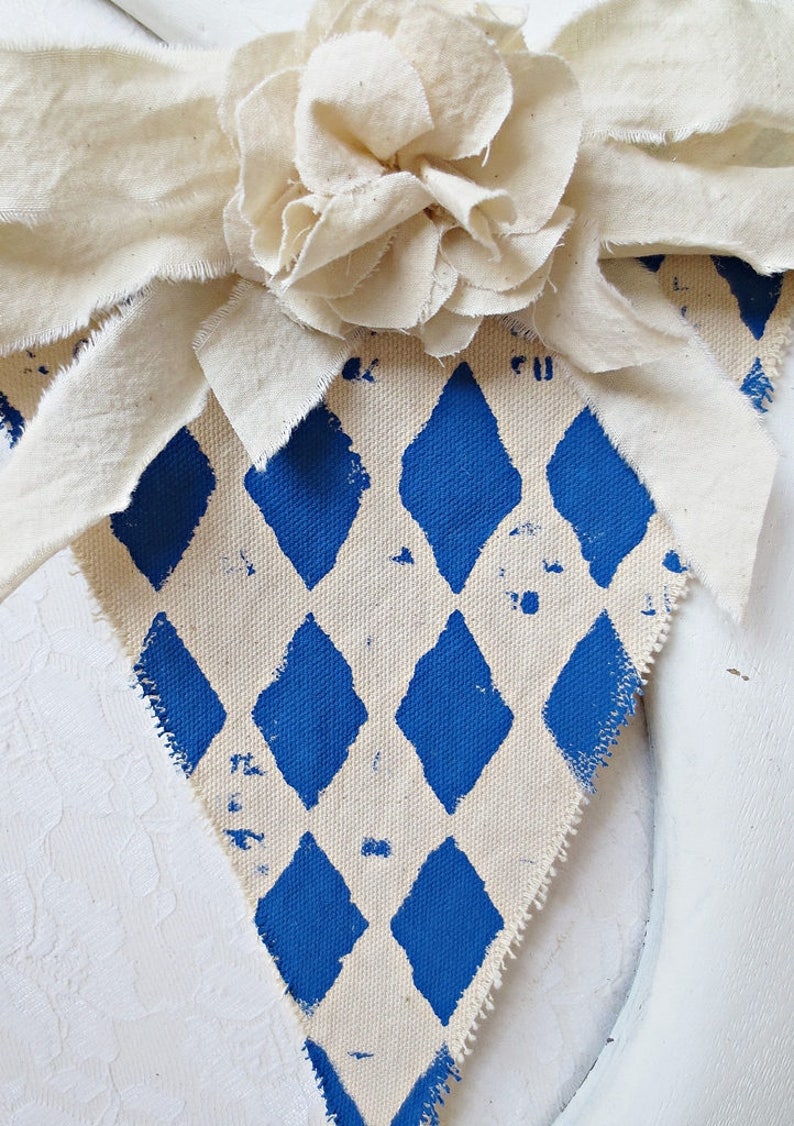 May include: A white fabric banner with a blue diamond pattern. The banner has a white fabric flower attached to the top.