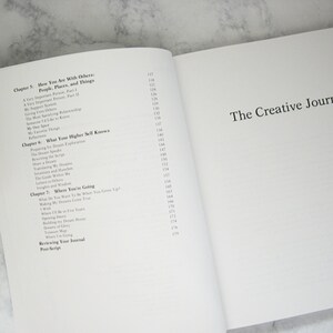 Peut inclure: Un gros plan sur un livre intitul&eacute; "The Creative Journal" avec une table des mati&egrave;res listant les chapitres et les num&eacute;ros de page. Les chapitres incluent "How You Are With Others", "What Your Higher Self Knows", et "Where You're Going".