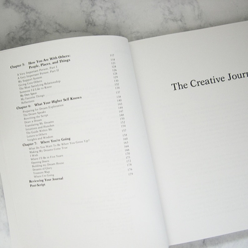 Peut inclure: Un gros plan sur un livre intitul&eacute; "The Creative Journal" avec une table des mati&egrave;res listant les chapitres et les num&eacute;ros de page. Les chapitres incluent "How You Are With Others", "What Your Higher Self Knows", et "Where You're Going".