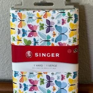 May include: A Singer fabric roll featuring a colorful butterfly pattern in shades of blue, yellow, pink, and green on a white background. The fabric is 36 inches by 44 inches. The Singer logo is displayed on a red band.