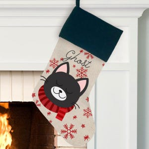 May include: A personalized Christmas stocking with a black cat wearing a red scarf and snowflakes. The stocking is made of burlap and has the name "Ghost" embroidered on it.