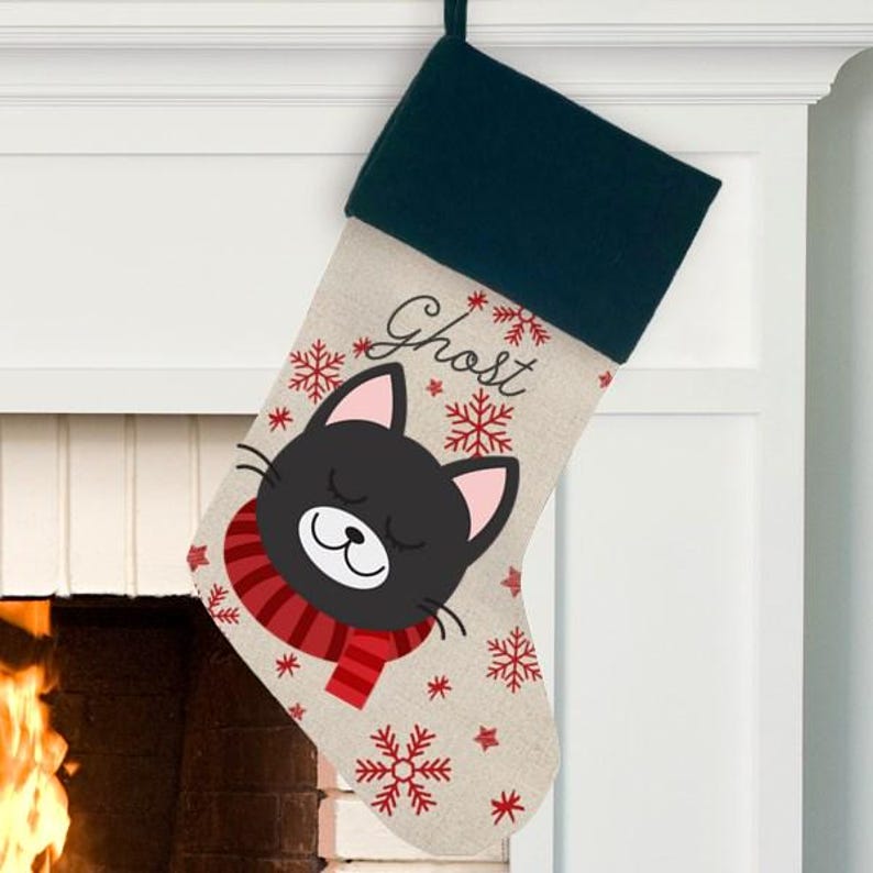 May include: A personalized Christmas stocking with a black cat wearing a red scarf and snowflakes. The stocking is made of burlap and has the name "Ghost" embroidered on it.