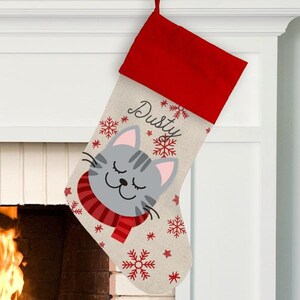 May include: Personalized Christmas stocking with a cute gray cat wearing a red scarf and snowflakes. The stocking is made of burlap and has the name "Dusty" embroidered on it.