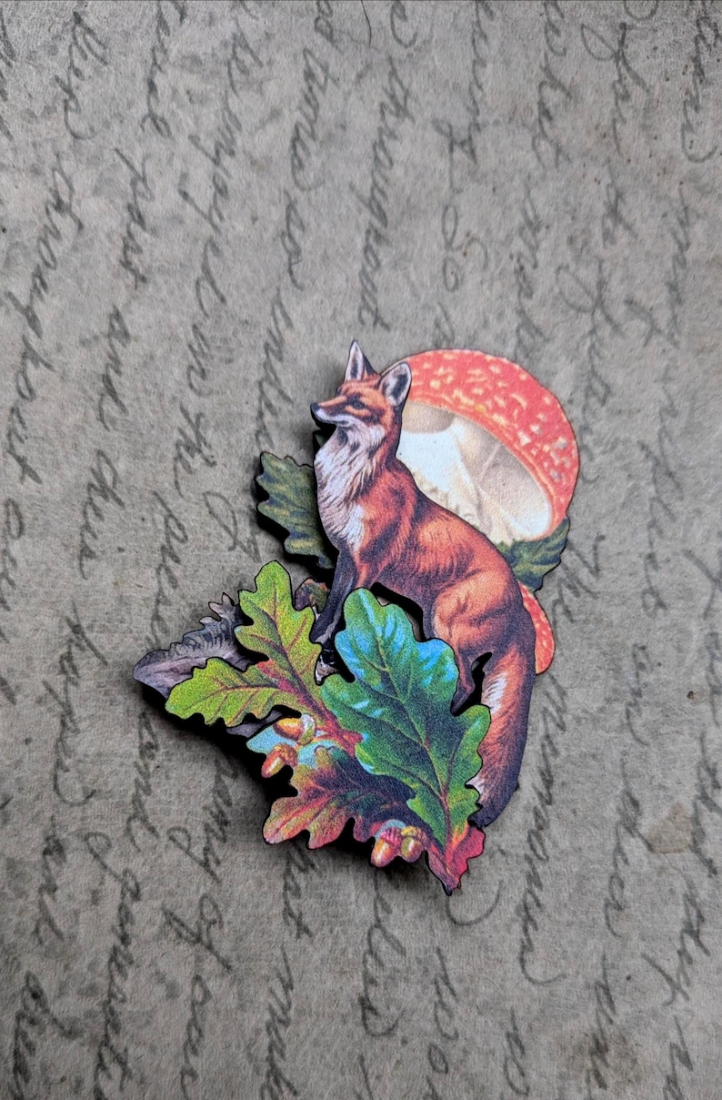 May include: A wooden fox figurine with a red and white mushroom and colorful oak leaves. The fox is orange and white, with a detailed design. The leaves are green, blue, and red. The background is a textured, tan surface.