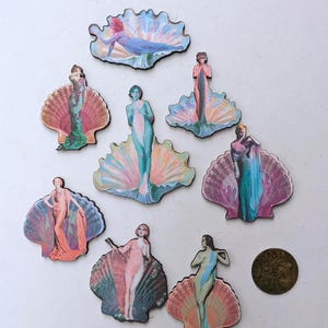 May include: A collection of wooden art deco-style mermaid figures, each depicted in a seashell. The mermaids are painted in pastel colors, with details like flowing hair and draped fabric. A vintage coin is also present.