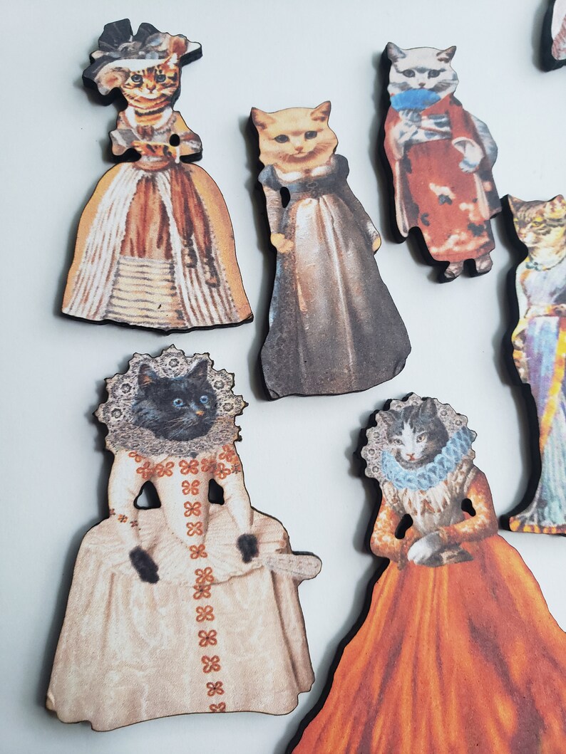 May include: A set of nine wooden ornaments featuring cats dressed in vintage clothing. The cats are wearing various colors and patterns, including red, white, blue, and black. The ornaments are perfect for adding a touch of whimsy to any home decor.