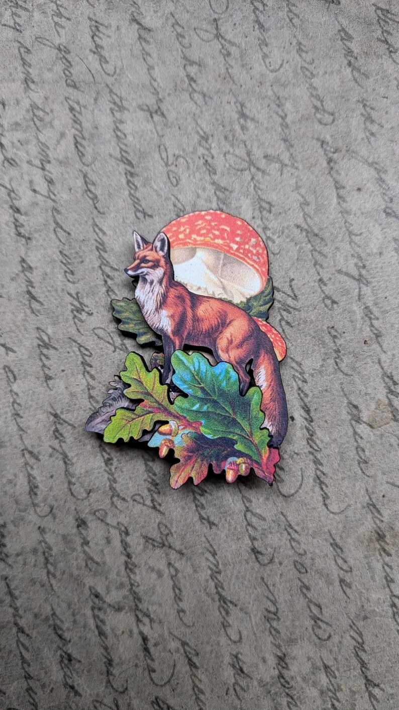 May include: A wooden fox figurine with a red and brown coat, standing on colorful leaves and a mushroom. The fox is facing left. The background is a vintage paper with handwritten text.