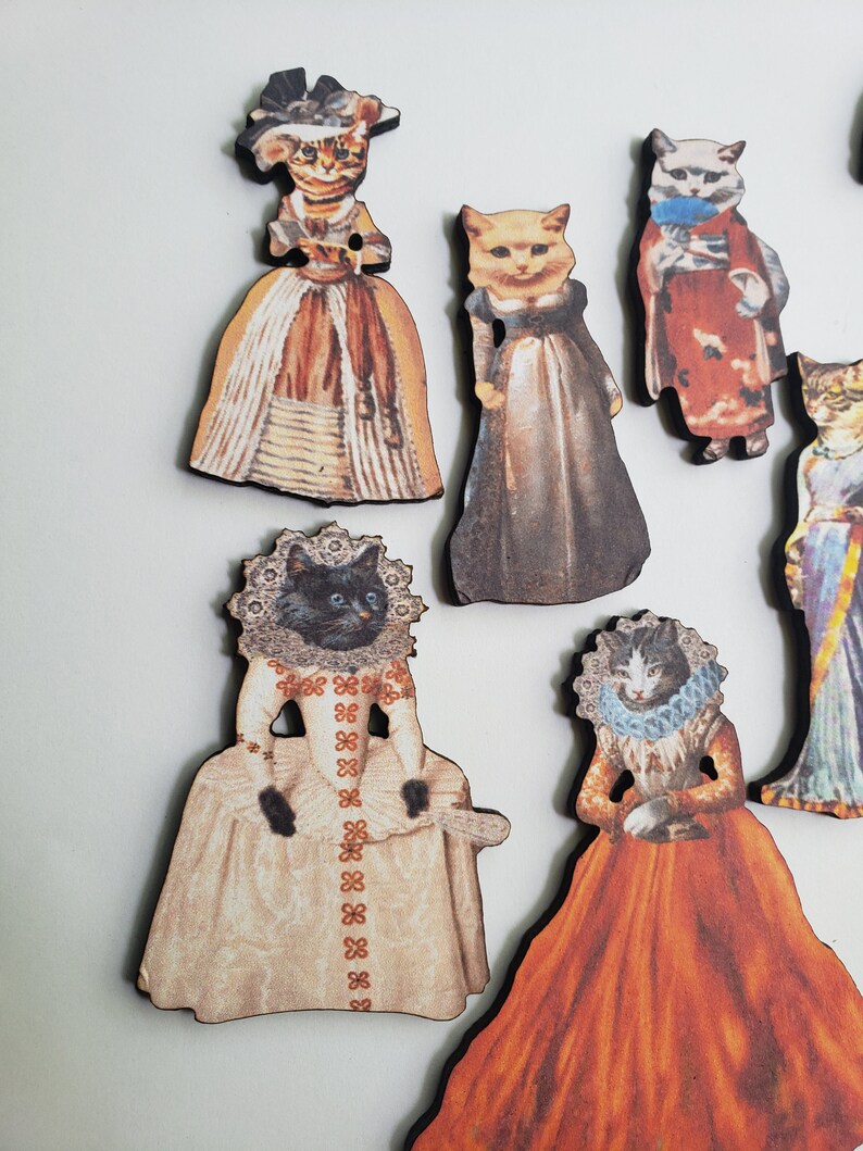 May include: Set of eight wooden ornaments featuring cats dressed in vintage clothing. The ornaments are painted with intricate details and feature a variety of colors, including brown, white, black, orange, and blue.