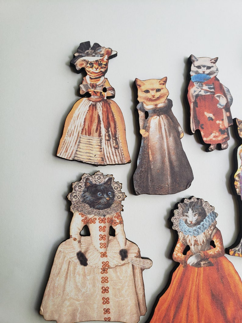 May include: Set of eight wooden cat figurines dressed in vintage clothing. Each figurine features a different cat breed with a unique outfit and pose. The figurines are painted in a variety of colors, including brown, white, black, and orange.