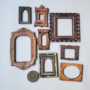 May include: A collection of nine decorative miniature picture frames in various shapes and sizes. The frames feature ornate designs with gold, brown, and green accents. A coin is also present.