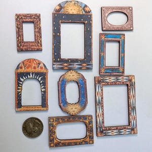 May include: A collection of decorative wooden frames in various shapes and sizes. The frames feature intricate designs with warm colors, including brown, blue, and gold. Some frames have arched tops, while others are rectangular or oval.