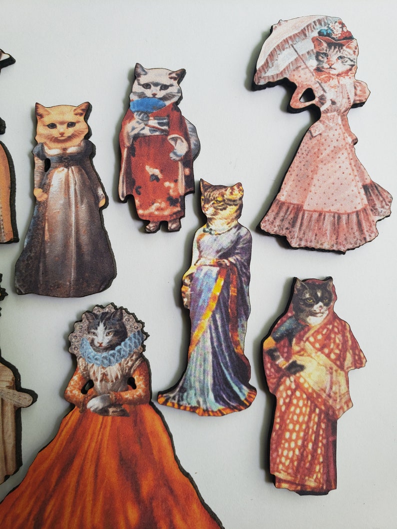 May include: A set of eight wooden cat figurines dressed in various vintage clothing. The cats are wearing dresses, suits, and a sari. Some of the cats are holding umbrellas and other accessories.
