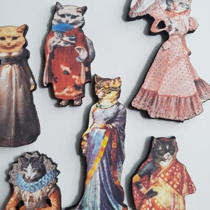 May include: Six wooden cat figurines dressed in different outfits. The cats are wearing a variety of clothing, including a kimono, a sari, and a Victorian dress. The figurines are all hand-painted and have a vintage look.