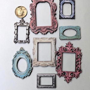 May include: A collection of ornate, vintage-style picture frames in various shapes and sizes. The frames feature colors like pink, blue, and cream, with intricate detailing. A gold-colored coin is also present.