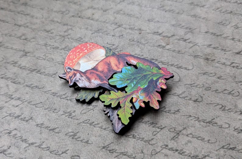 May include: A wooden fox figurine with a red and white mushroom and colorful leaves. The fox is brown and orange, and the leaves are green, blue, and yellow. The background is a textured, gray surface with handwritten text.
