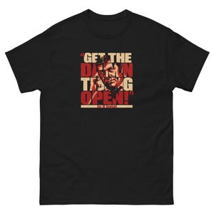 May include: A black short-sleeved t-shirt featuring a graphic print of a man on a telephone with the text "GET THE DAMN THING OPEN!" in red and beige lettering, with the name "Jim 'JR' Rowland" printed in a beige bar at the bottom.