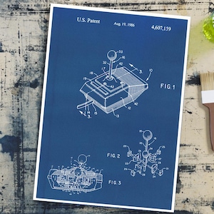 May include: A blueprint of a joystick patent from August 19, 1986, with detailed diagrams labelled FIG. 1, FIG. 2, and FIG. 3. The print, with white borders, shows the joystick's design. The background is a distressed wooden surface.