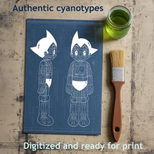 May include: A blue print with two white illustrations of a robot character. The text "Authentic cyanotypes" and "Digitized and ready for print" are displayed. A jar of green liquid and a paintbrush with a wooden handle are also visible.
